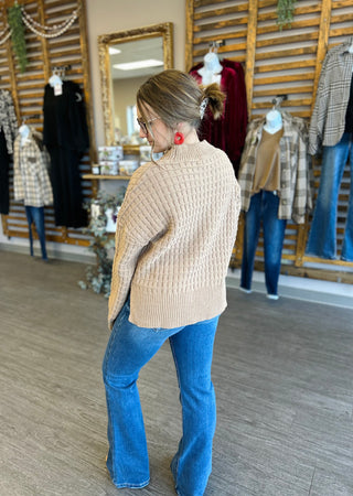 Woman wearing textured knit sweater and jeans in clothing boutique, shown from behind.