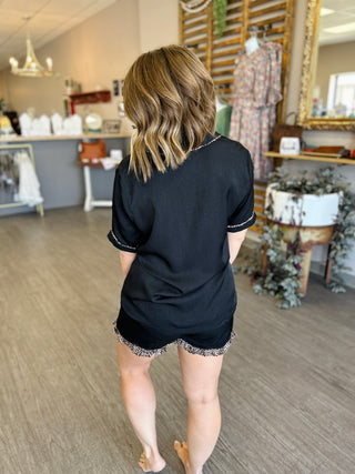 Woman wearing black pajama set with white trim, shown from behind in boutique setting.