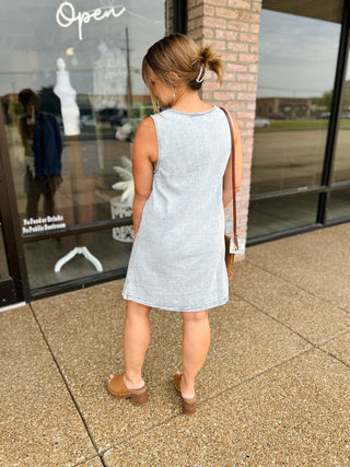 Woman wearing a sleeveless denim mini dress with relaxed fit, styled with heeled mules and crossbody bag.