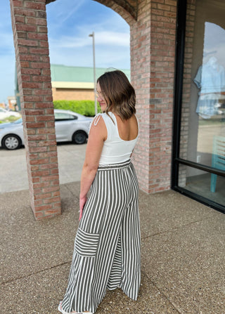 Woman wearing white sleeveless tie-shoulder top with striped wide-leg pants, standing outside brick storefront.