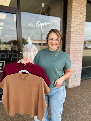 Woman wearing Zenana Short Refined Rib Sweater Top outside boutique, holding additional color options on hangers.