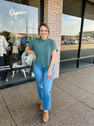 Woman wearing a ribbed mock neck short sleeve cropped sweater top paired with jeans outdoors.