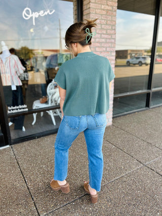 Woman wearing a cropped ribbed sweater top paired with straight-leg jeans and clogs.