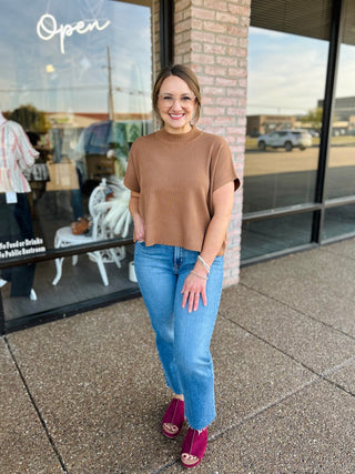 Woman wearing a ribbed short sleeve mock neck sweater top, paired with jeans outdoors.