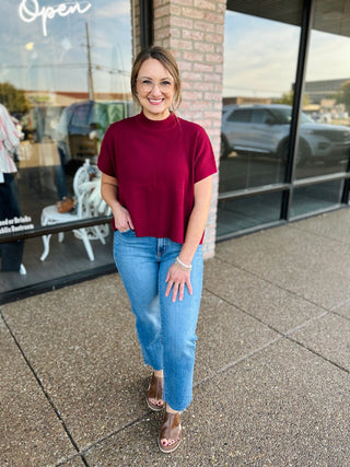 Woman wearing a mock neck short sleeve ribbed sweater top paired with light wash jeans and sandals.
