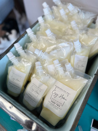 Collection of squeezable wax melt pouches with white caps displayed in metal container, featuring Chai Tea scent.