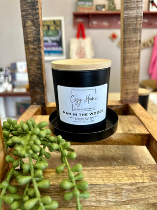 Black soy candle with wooden lid and wick displayed on rustic wooden shelf with green succulent plant.
