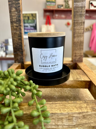 Black soy candle with wooden lid and white label on rustic wooden display with green succulent plant.