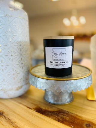 Black soy candle with wooden wick displayed on decorative metal cake stand with white ceramic vase