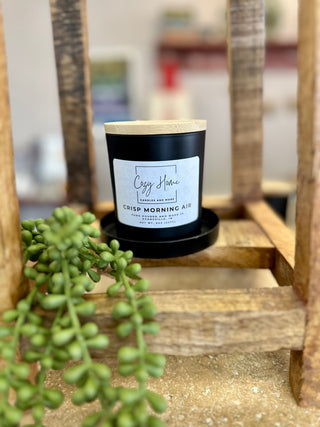 Black soy candle with wooden lid sits on wooden ladder shelf next to green succulent plant.