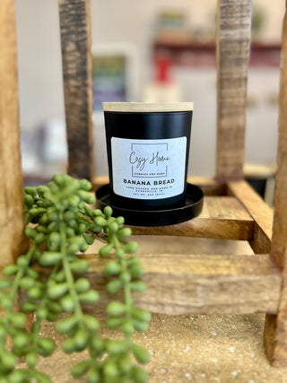 Black soy candle with wooden wick displayed on rustic wooden shelf with green succulent plant