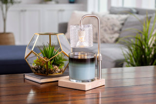 Silver candle warmer lamp with textured glass shade melting layered candle on wooden table