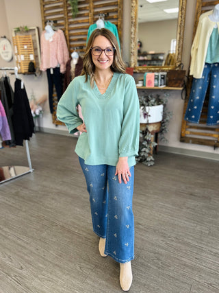 Woman wearing mint green v-neck top with balloon sleeves and embellished jeans in boutique setting