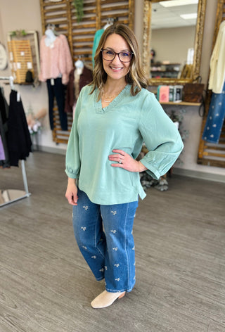 Woman wearing mint green v-neck top with embroidered jeans in clothing boutique setting