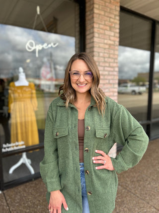 Woman smiling outside boutique wearing an open corduroy shacket over a neutral top with jeans.