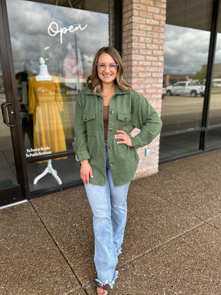 Woman wearing an open button-front corduroy shacket over a brown top and jeans.