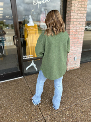 Woman wearing an oversized ribbed shacket with light wash jeans, shown from behind outside a boutique.