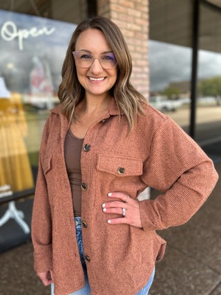 Woman smiling outdoors wearing an oversized button-front shacket with chest pocket and jeans.