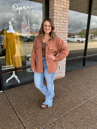 Woman smiling outside boutique wearing an open button-front shacket over a fitted top and jeans.