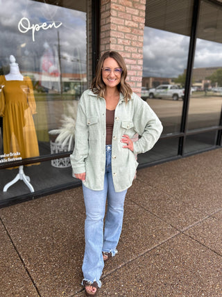 Woman wearing a relaxed corduroy button-up shacket over jeans and sandals outside boutique.