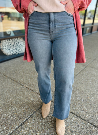 Woman wearing smoke grey high rise straight leg jeans with coral cardigan and nude flats.