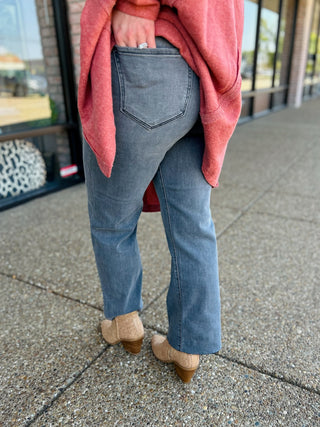 Woman wearing straight-leg jeans with coral sweater and tan heeled boots walking on sidewalk