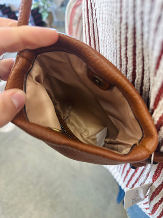 Interior view of a small leather crossbody bag showing tan fabric lining and snap pocket.
