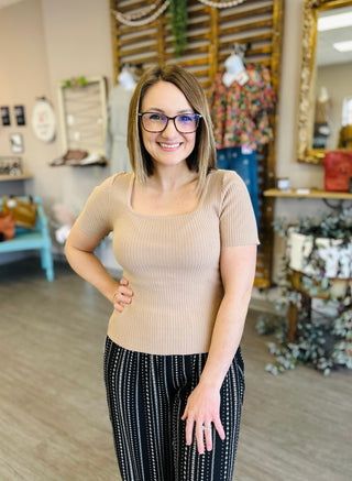 Woman wearing beige ribbed square neck top and patterned pants in clothing boutique store