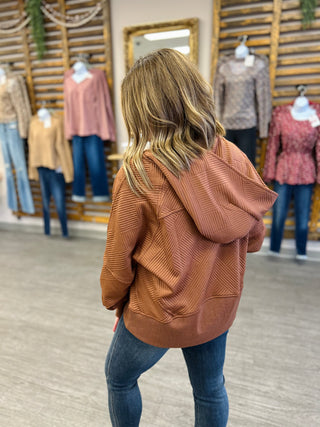 Woman wearing textured hoodie and jeans in clothing store with racks of apparel in background.