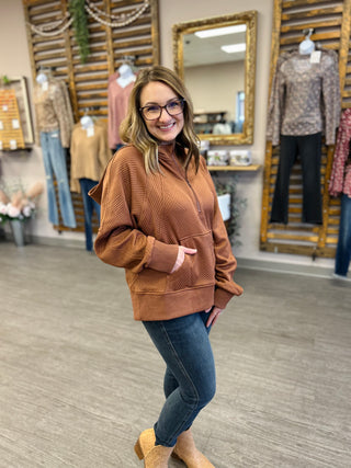 Woman wearing brown ribbed hoodie with jeans and boots in clothing boutique store
