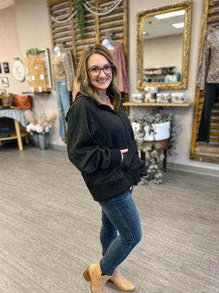 Woman wearing black ribbed hoodie with tie waist and jeans in clothing boutique setting