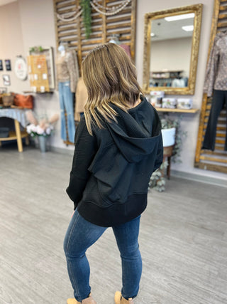 Woman wearing navy blue ribbed hoodie with jeans, shown from behind in casual retail setting.