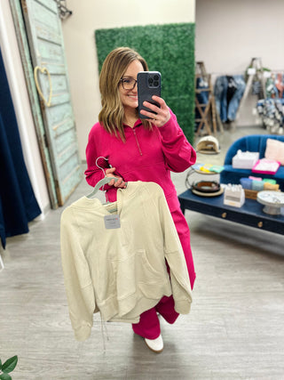 Woman in pink ribbed matching set taking mirror selfie while holding cream colored garment in boutique store