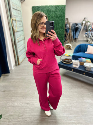 Woman wearing pink ribbed matching sweatsuit set taking mirror selfie in retail store