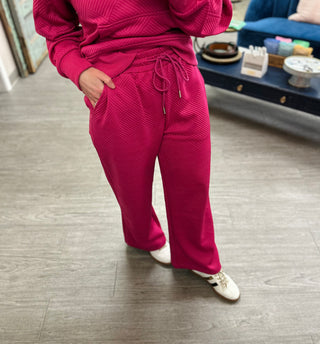 Person wearing pink ribbed knit loungewear set with drawstring pants and matching top in modern kitchen setting.