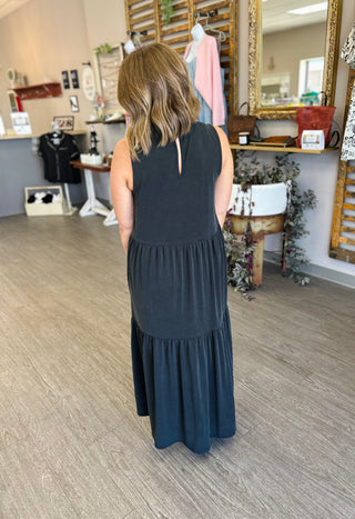 Woman wearing sleeveless tiered maxi dress in retail boutique setting, shown from behind.