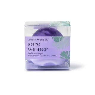 Purple body massager with roller ball in clear packaging with lavender and tropical leaf design.