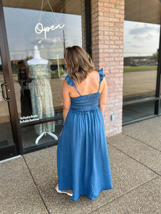 Woman wearing a smocked bodice maxi dress with ruffle straps, standing outside a boutique.