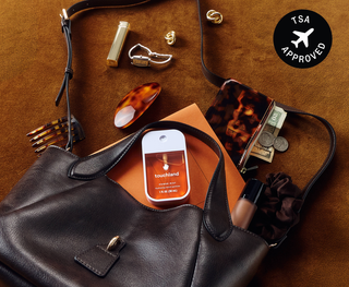 Touchland Power Mist hand sanitizer resting in an open leather handbag with everyday essentials scattered around.