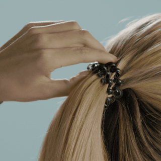 Hand holding blonde hair in ponytail secured with clear spiral hair coil tie