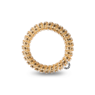 Spiral coiled hair tie in metallic gold color with brand tag on black background