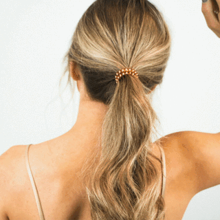 Woman wearing blonde ponytail with gold spiral hair coil tie, back view showing hairstyle