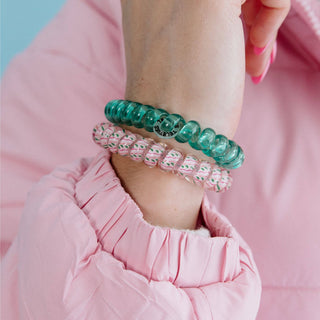 Person wearing two spiral hair coils on wrist, one teal and one pink with pattern, in pink outfit.