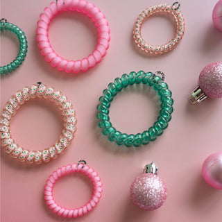 Colorful spiral hair coils and festive ornaments arranged on pink background showcasing hair tie accessories