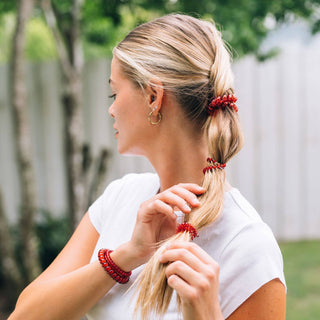 Woman with blonde hair styled in ponytail using red spiral hair coils as hair ties.