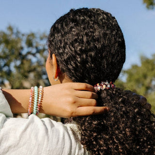 Woman with curly hair wearing colorful beaded bracelets and a patterned spiral hair coil in ponytail.