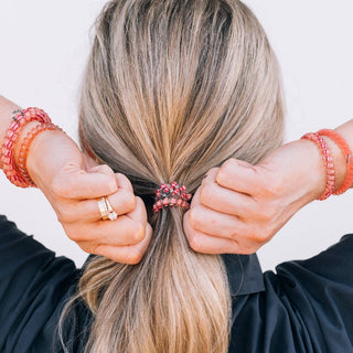 Woman securing ponytail with orange spiral hair coil, wearing matching beaded bracelets
