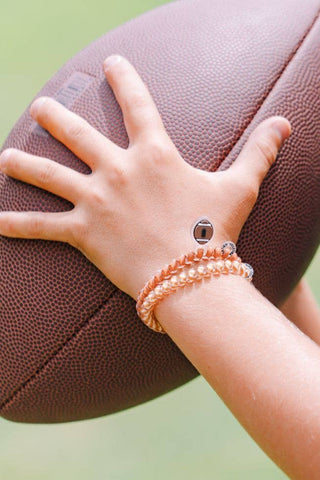 TELETIES football charm spiral hair coils worn as bracelets on wrist holding a football.
