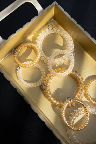 TELETIES spiral hair coils arranged on a gold decorative tray against a dark background.