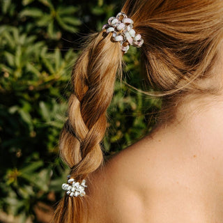 Woman wearing braided ponytail with white beaded spiral hair coils against green foliage background